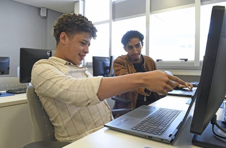 Os fundadores da GenMek trabalhando juntos em um notebook no laboratório de informática