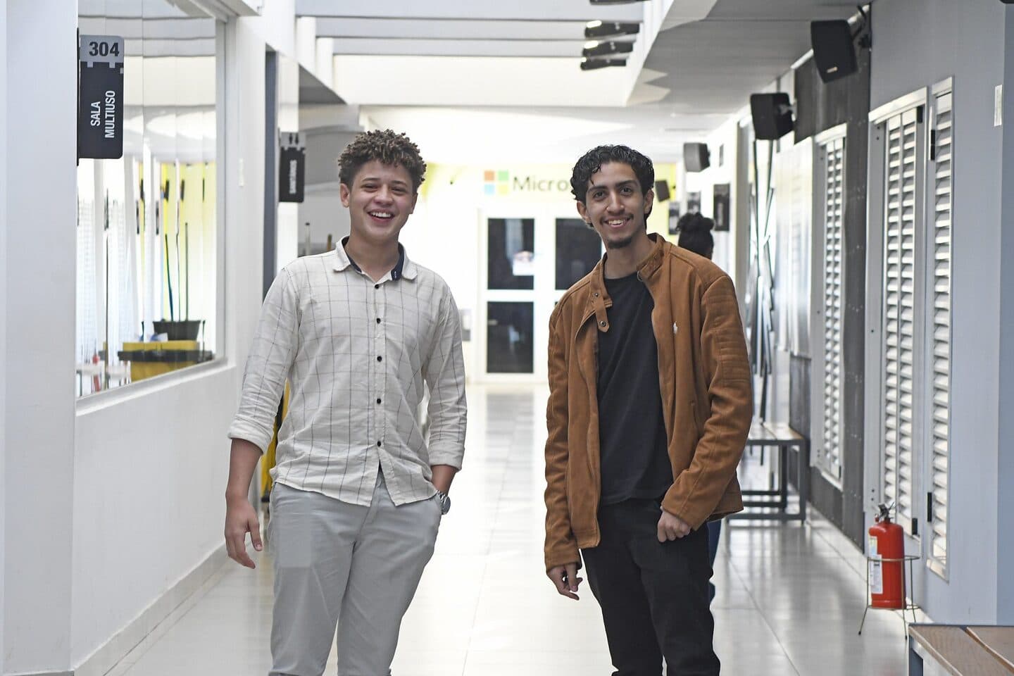 Evandro Castro Marques e Marlon Santana de Oliveira, fundadores da GenMek, sorrindo no corredor do Senac em Campo Grande